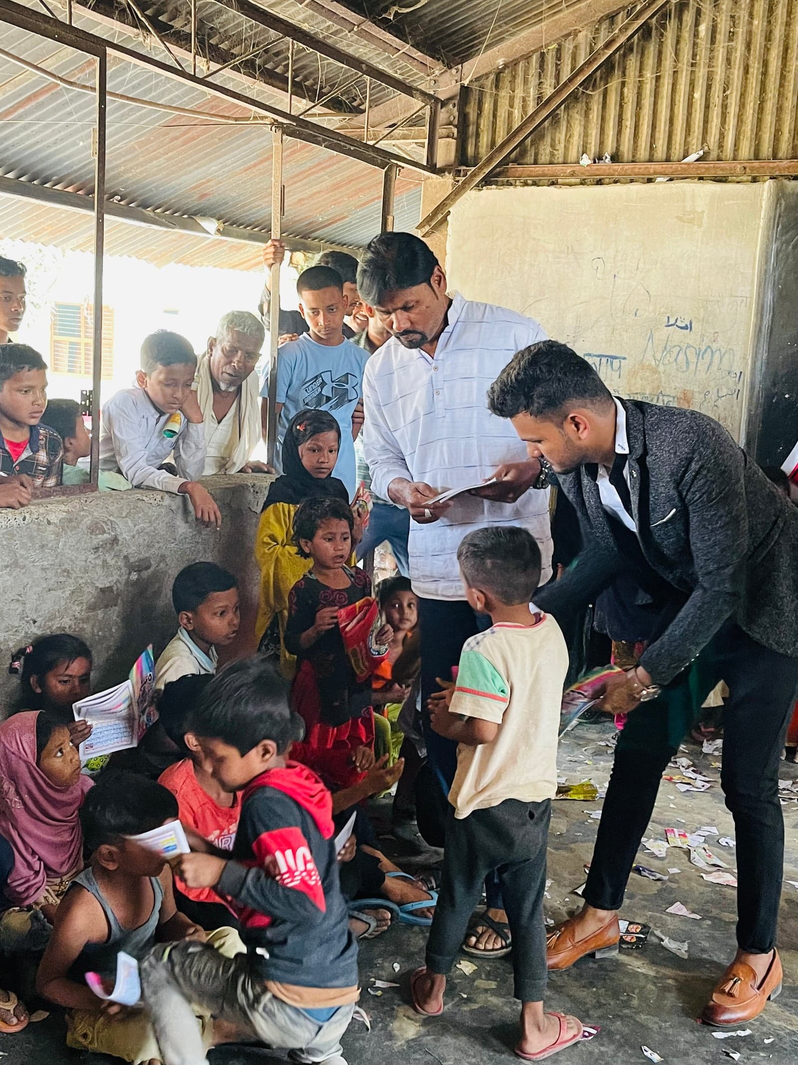 Adults distribute printed learning materials among a group of children.