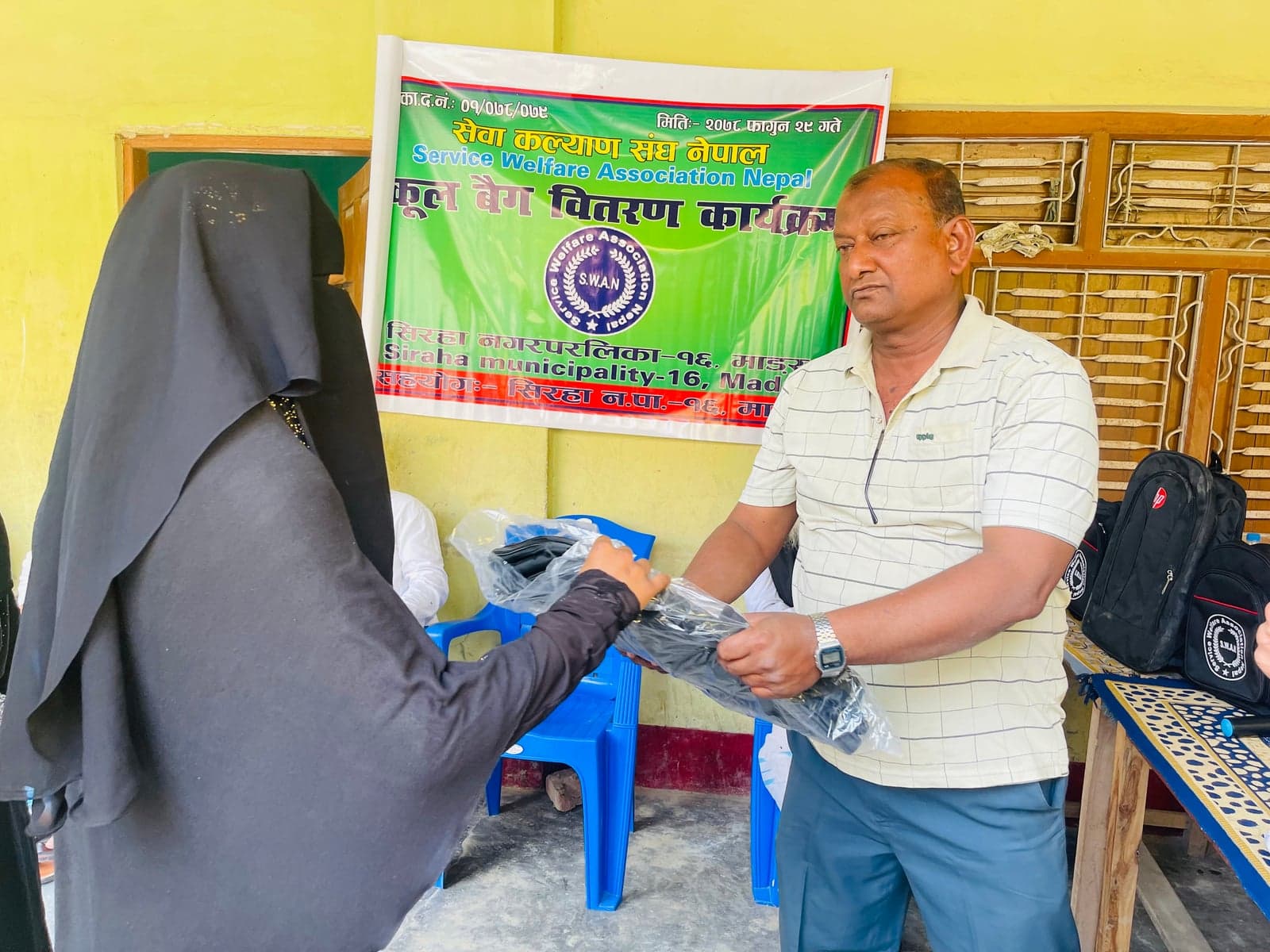 A participant receives a wrapped school bag in front of a SWAN banner.