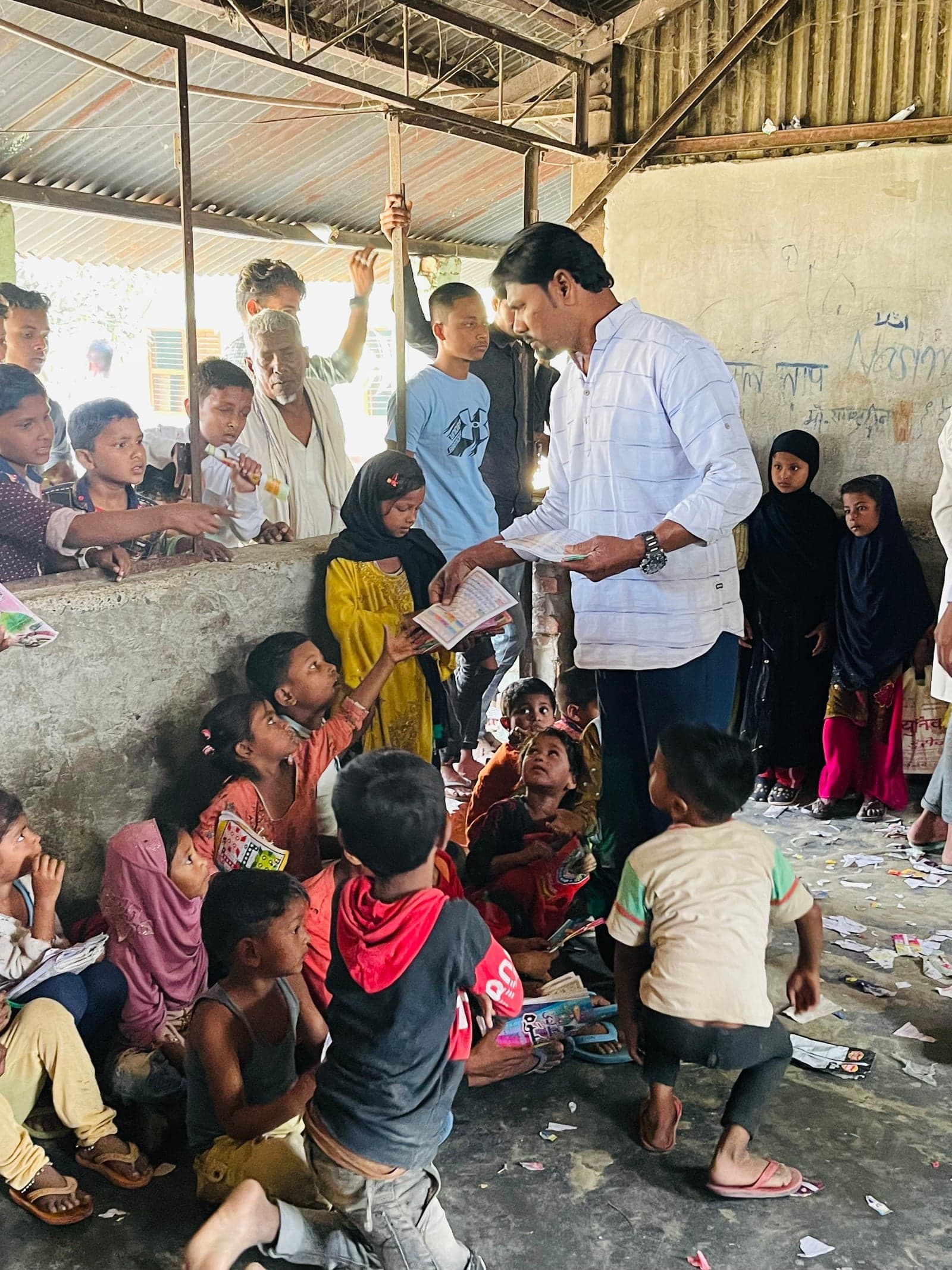 An adult hands printed learning materials to children gathered indoors.